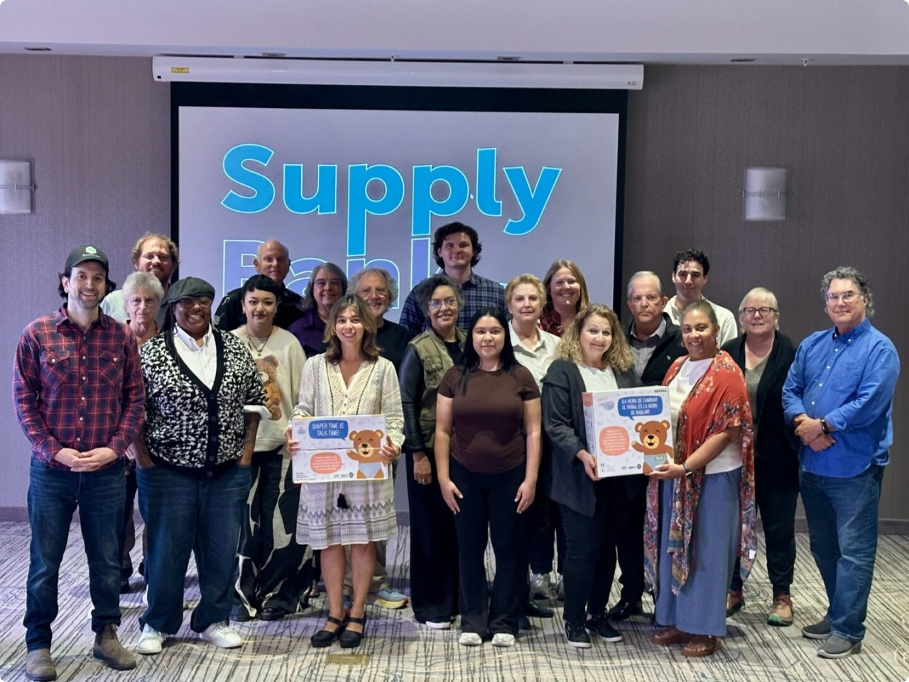 Group photo of community partners standing in front of SupplyBank presentation screen