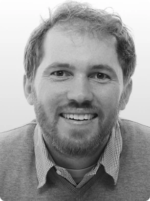 Black and white professional headshot of friendly bearded man in business attire